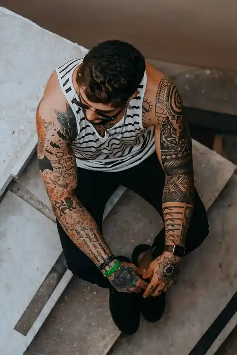 Sleeve tattoos down both arms of a man who is sitting down