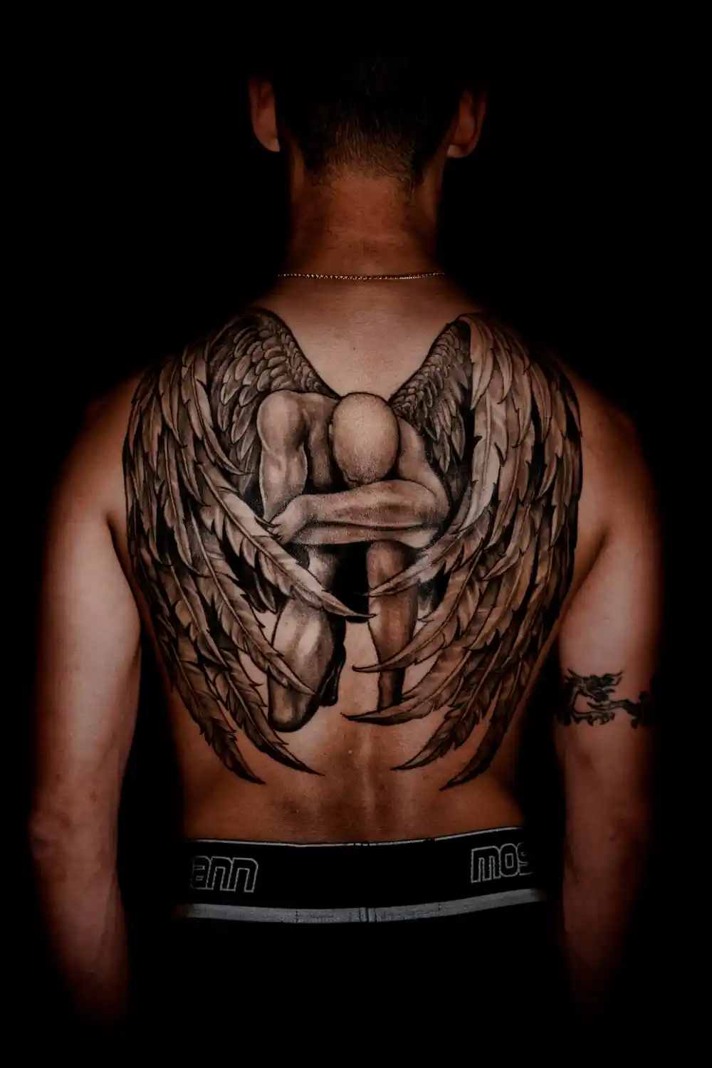 A tattoo of a man on his knees with angel wings on his back