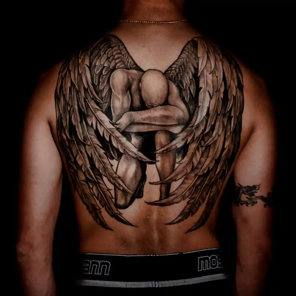 A tattoo of a man on his knees with angel wings on his back