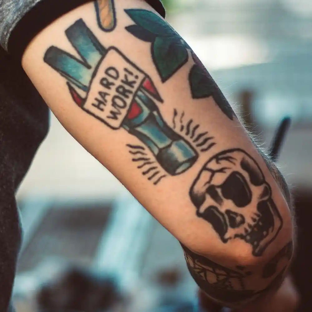 A colourful tattoo of a hammer head with the text 'hard work'